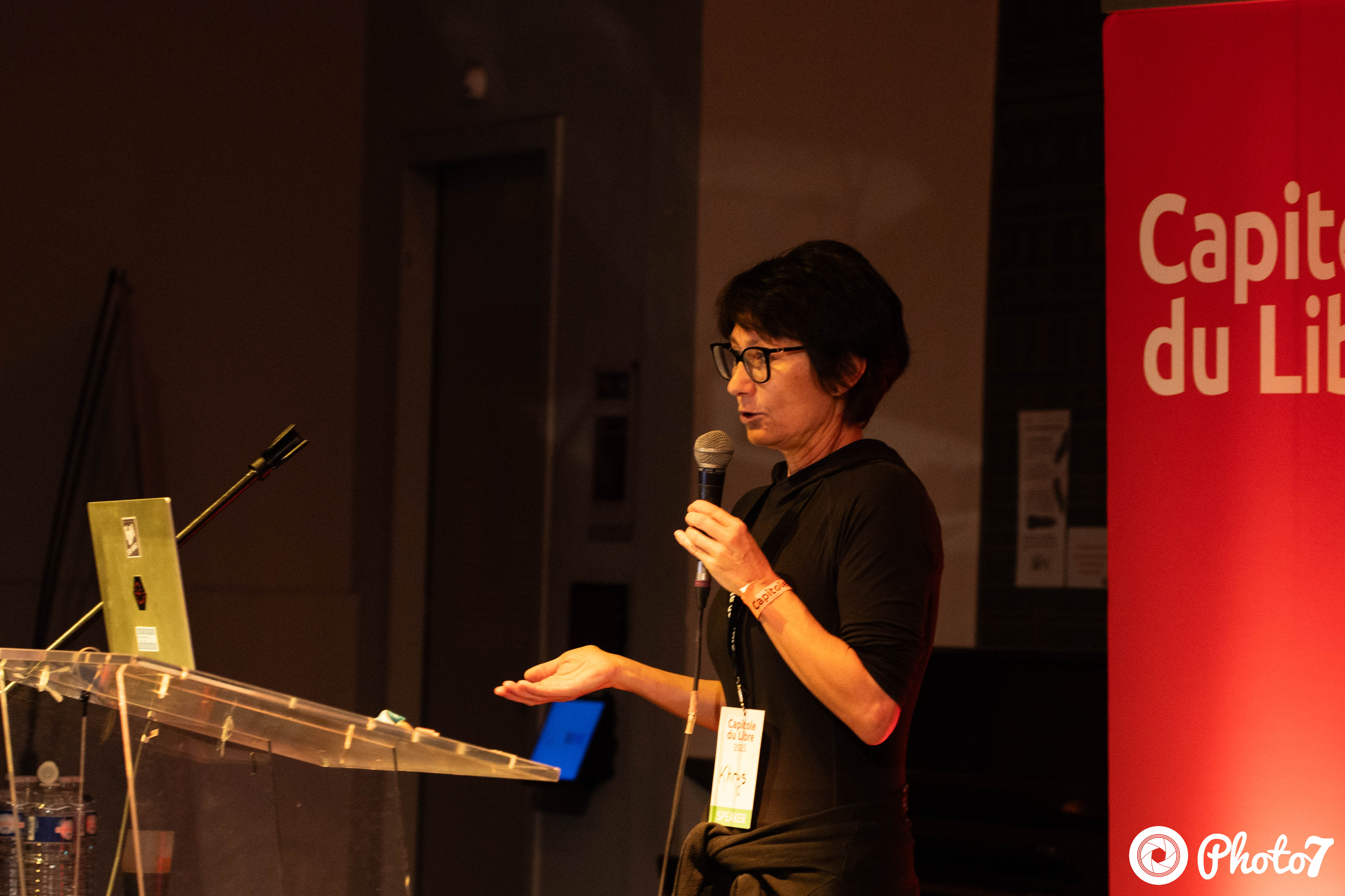 Speakerine au pupitre avec le banner Capitole du Libre en arrière-plan